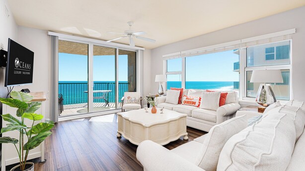 A spacious living room with a large sliding glass door leading to a balcony, a ceiling fan, a flat-screen TV, and a potted plant. - Oceanfront | Heated Pool-Twin Towers #504 (Daytona Beach Shores)