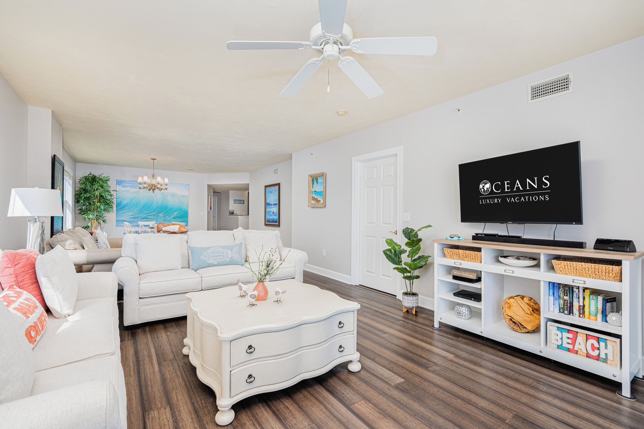 A living room with a white sofa, a white coffee table, a white TV stand, and a ceiling fan.