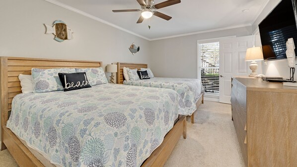 A bedroom with two beds, a ceiling fan, a desk with a lamp, and a view of the outside through a window with blinds. - 2 BR, ground floor on Golf Course with Pool! (Pawleys Island)