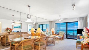 A spacious living room with wicker furniture, a glass table, and a large window offering a view of the ocean.