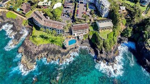 An aerial view of a coastal property with a large building, a swimming pool, and clear turquoise waters.