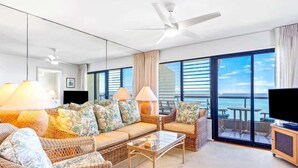 A spacious living room with wicker furniture, a glass coffee table, and a large window offering a view of the ocean.