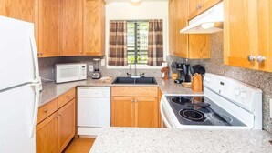 Une cuisine compacte avec des meubles en bois, un réfrigérateur blanc, un four à micro-ondes, un lave-vaisselle, une cuisinière et une fenêtre avec des rideaux.