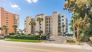 A multi-story hotel with a central courtyard, palm trees, and a clear sky. - Sand Castle III 201 - GULFFRONT SPIRAL STAIRCASE! (Indian Shores)