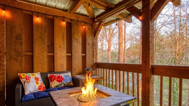 A covered outdoor seating area with a fire feature, wooden beams, and a view of trees. - Romance abounds!♥Hot Tub♥Whirlpool Bath♥Comm Pool♥Fire Table (Townsend)