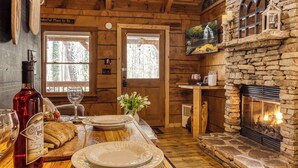 Un interior de madera con chimenea de piedra, vigas de madera en el techo y un comedor con mesa de madera dispuesta para dos.