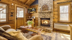 A log cabin interior with a stone fireplace, wooden walls, a bench, and a cozy seating area. - Romance abounds!♥Hot Tub♥Whirlpool Bath♥Comm Pool♥Fire Table (Townsend)