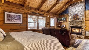 A log cabin interior with a fireplace, a bed, and a stone wall. - Romance abounds!♥Hot Tub♥Whirlpool Bath♥Comm Pool♥Fire Table (Townsend)