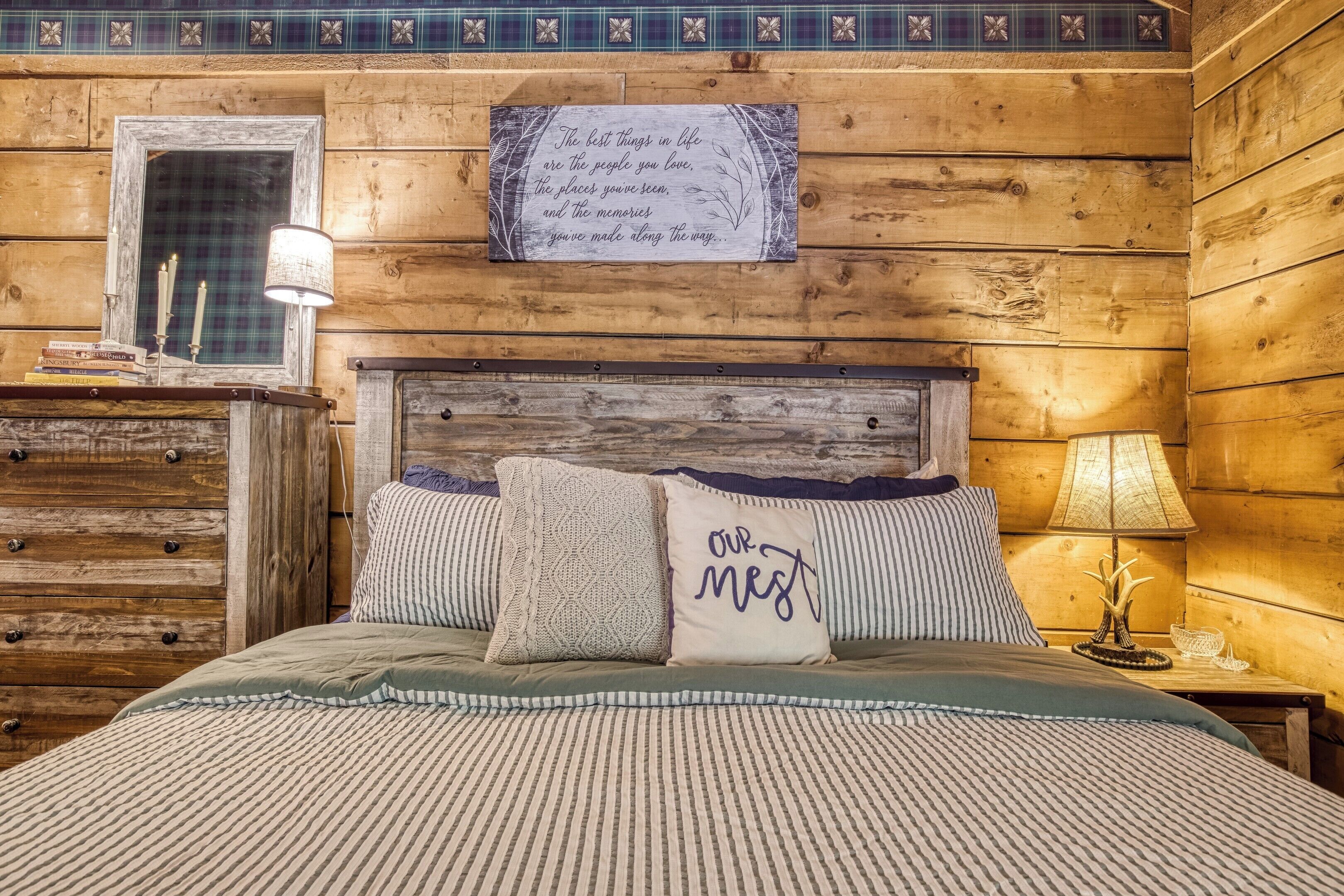 Ein schlicht eingerichtetes Schlafzimmer im Chalet-Stil mit Bett, Kissen, Nachttisch, Lampe, Spiegel und einem an der Wand befestigten Schild.