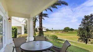 A covered patio with a round table and chairs, overlooking a well-maintained lawn and golf course. - Beautiful Townhome Near Attractions with Stunning Views of The Palmer Golf Course (Kissimmee)
