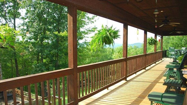 Eine überdachte Terrasse mit Holzgeländern, grünen Bänken und Blick auf üppiges Grün.