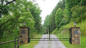 Ein begrenzter Zugang zu einer Anlage namens 'River Mountain Estates' mit einem Kiesweg, der durch ein bewaldetes Gebiet führt.