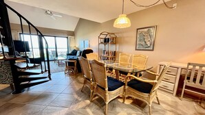Un coin repas avec des chaises en osier et une table en verre, un escalier et une vue sur un balcon.
