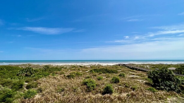 Un paysage côtier avec un ciel dégagé, une plage de sable et une promenade en bois menant à la mer.