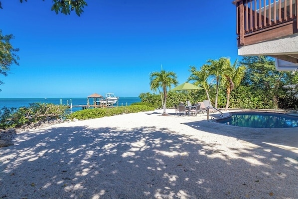 A pool area with a view of the ocean, a wooden deck, and a lounge chair.