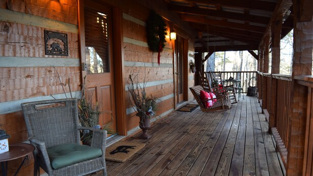 Une véranda en bois avec des fauteuils en osier, une petite table et une plante en pot.