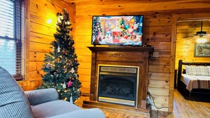 L’intérieur d’un chalet chaleureux, avec une cheminée, un sapin de Noël et un téléviseur fixé au-dessus de la cheminée.