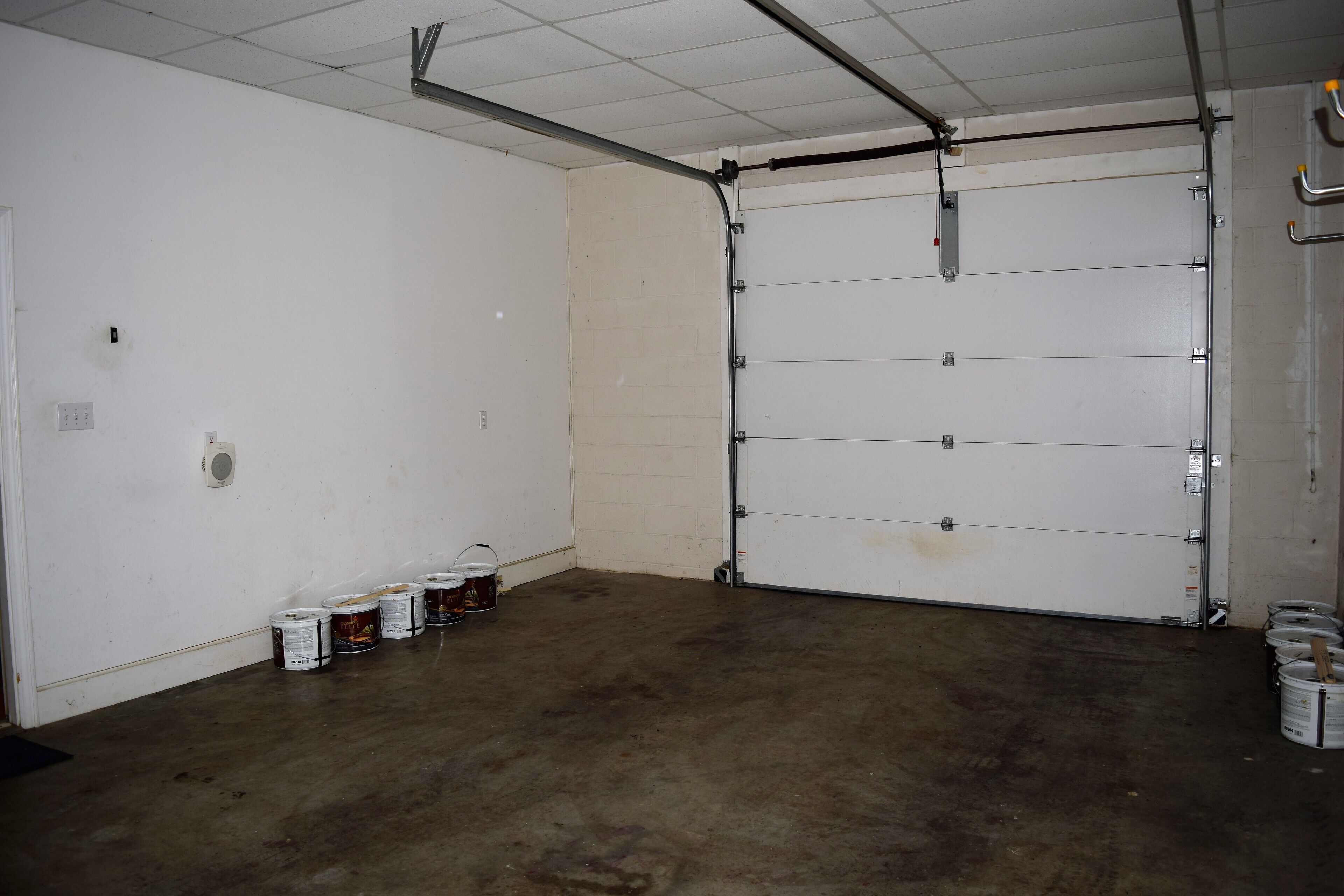 A garage with a closed door, concrete floor, and several paint cans against the wall.