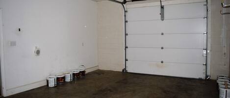A garage with a closed door, concrete floor, and several paint cans against the wall.