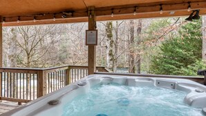 Ein Whirlpool unter einer Holzterrasse mit Blick auf einen Wald und einen Fluss.