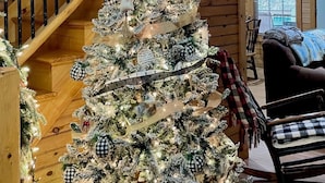 A Christmas tree decorated with white and black ornaments, ribbons, and lights, positioned in a wooden interior with a staircase and a cozy seating area. - River Access ☀Easy Access ☀Hot Tub ☀Sleeps 4 ☀Well Equipped (Townsend)