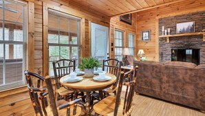 A cozy cabin interior with a dining table set for four, surrounded by wooden chairs, a fireplace, and a stone accent wall. - River Access ☀Easy Access ☀Hot Tub ☀Sleeps 4 ☀Well Equipped (Townsend)