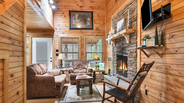 A cozy cabin interior with wooden walls, a stone fireplace, leather furniture, and a mounted TV. - River Access ☀Easy Access ☀Hot Tub ☀Sleeps 4 ☀Well Equipped (Townsend)