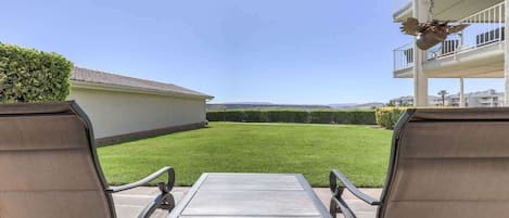 An outdoor patio with two metal chairs and a table, overlooking a well-maintained lawn and a distant view of a residential area.