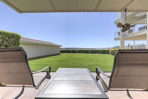 Una terrazza esterna con due sedie in metallo e un tavolo, con vista su un prato curato e una zona residenziale in lontananza.
