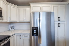 Frigorifero in acciaio inox con erogatore d'acqua, mobili da cucina bianchi e un forno a microonde sopra.