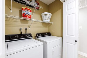A laundry room with two washing machines, a basket on a shelf, and a bag of detergent. - Las Palmas Resort #401 | All-Inclusive Amenities (Saint George)
