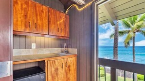 A kitchen with wooden cabinets and a view of the ocean through a sliding door. - Kona-Keauhou Sunsets+Style! Full Kitchen, Washer/Dryer, WiFi, Lanai, DVD, TV Kanaloa 2106 (KAILUA-KONA)