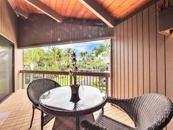 Un balcón con mobiliario de mimbre y una mesa de vidrio, con vistas a un jardín tropical.