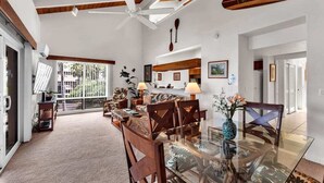 A spacious living room with a glass dining table, wooden chairs, and a ceiling fan. - Kona-Keauhou Sunsets+Style! Full Kitchen, Washer/Dryer, WiFi, Lanai, DVD, TV Kanaloa 2106 (KAILUA-KONA)