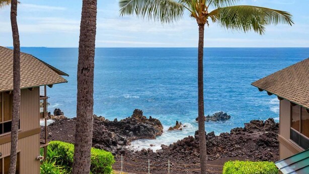 A coastal view with a wooden building, palm trees, and the ocean. - Kona-Keauhou Sunsets+Style! Full Kitchen, Washer/Dryer, WiFi, Lanai, DVD, TV Kanaloa 2106 (KAILUA-KONA)