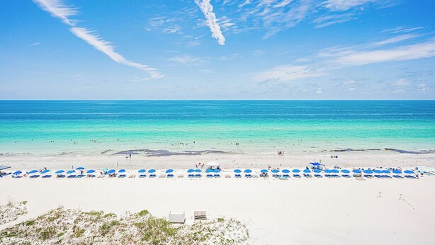 Ein Strand mit klarem türkisblauem Wasser, weißem Sand und einer Reihe blauer Sonnenschirme.