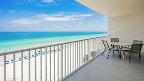 Ein Balkon mit Blick auf Strand und Meer. Ein Tisch mit Stühlen und einem Geländer sind vorhanden.