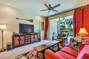 Un salón con televisión, mueble de madera, cortinas rojas, ventilador de techo y vistas a un jardín.