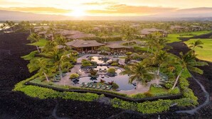 Un resort con varias edificaciones, un área de piscina central y palmeras circundantes.