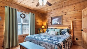 A cozy cabin bedroom with a wooden ceiling, a bed with patterned bedding, a bench, and a window with curtains. - Hot Tub❅Wood Fireplace❅King Bed❅Cozy - BEAR'S DEN (Townsend)