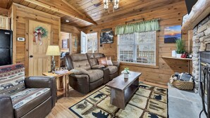 A cozy cabin interior with a wooden ceiling, a fireplace, a sofa, a recliner, and a dining table. - Hot Tub❅Wood Fireplace❅King Bed❅Cozy - BEAR'S DEN (Townsend)
