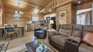 Ein gemütliches Blockhaus-Interieur mit Holzwänden, einem Essbereich mit Tisch und Stühlen, einer Couch und einer Küche mit Kühlschrank und Schränken.