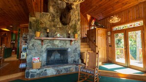A rustic interior with a stone fireplace, wooden beams, and a large antler mounted on the wall. - Mountain Cabin,180* View,HotTub,SpaTub,Pool Table,WiFi (Ferguson)