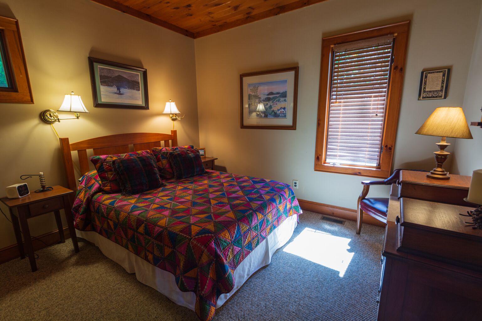A bedroom with a wooden bed, two bedside lamps, a desk with a lamp, and a window with blinds.