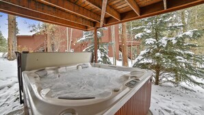 A hot tub under a wooden pergola with snow-covered trees and a red building in the background. - Beautiful half duplex home, recently remodeled with garage and private hot tub!! (Frisco)