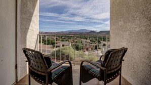 Un balcón con dos sillas frente a vistas de una zona residencial y montañas.