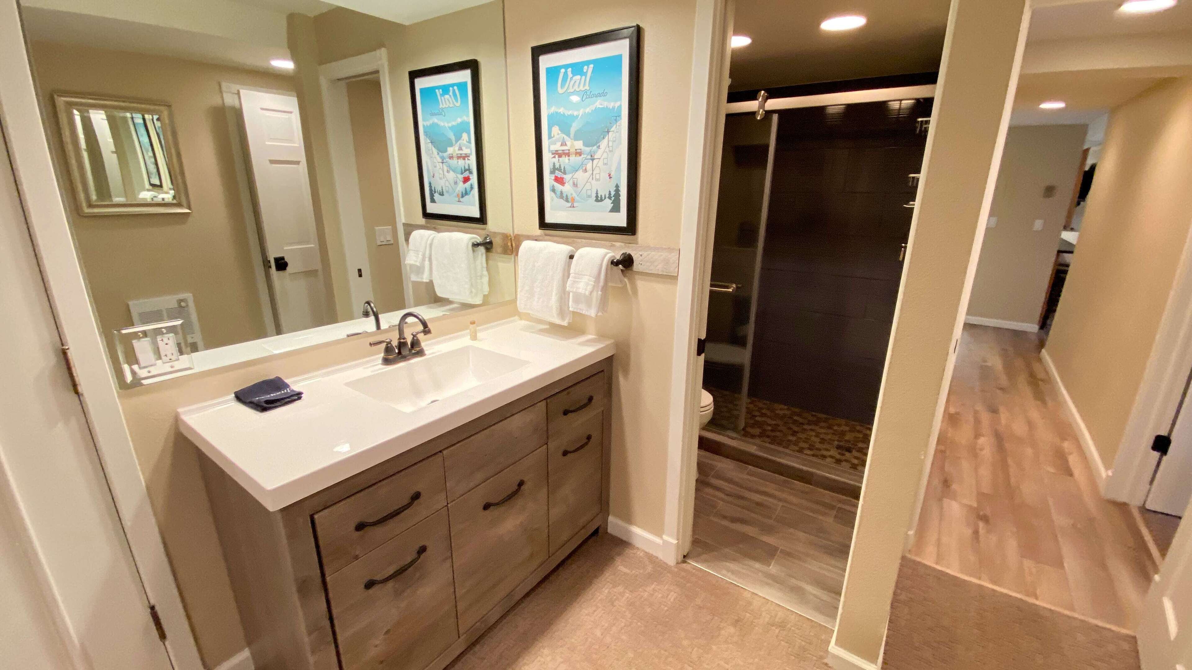 A modern bathroom with a large mirror, two framed pictures, a sink, and a shower area.
