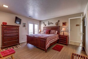 A bedroom with a large bed, wooden dresser, and a television on the wall.
