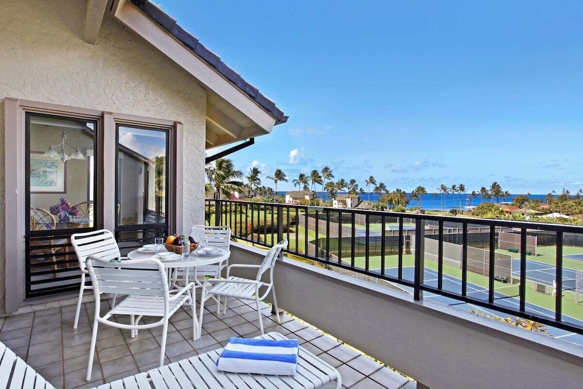 A balcony with a table and chairs, a view of a tennis court, and palm trees.