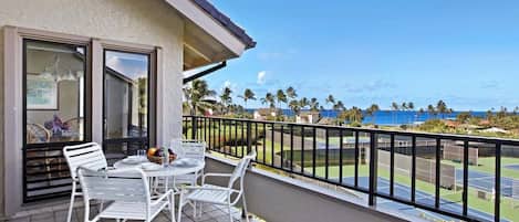 A balcony with a table and chairs, a view of a tennis court, and palm trees.